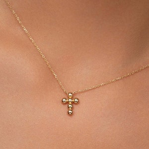 May include: A delicate gold necklace with a small cross pendant made of tiny gold beads.