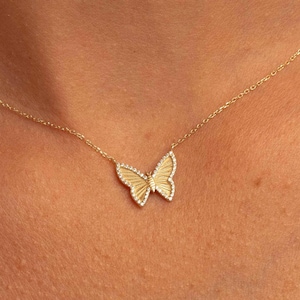 May include: A delicate gold chain necklace with a small, detailed butterfly pendant. The butterfly is made of gold and has a textured surface. The pendant is accented with small, clear stones.
