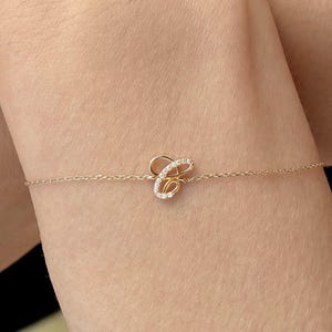 May include: Gold-toned bracelet featuring a cursive letter "C" embellished with small, sparkling stones. The delicate chain bracelet is displayed on a person's arm, showcasing the jewelry's elegant design.