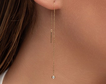 May include: Gold chain earrings with a small diamond at the end of the chain. The earrings are dangling from the earlobe.
