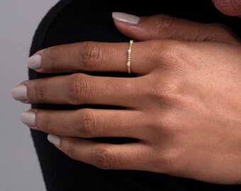 May include: A delicate gold ring with small, clear stones set in a beaded band.