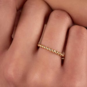 Könnte beinhalten: Ein goldener Perlenring an einem Finger. Der Ring besteht aus kleinen, runden Perlen, die gleichmäßig verteilt sind.