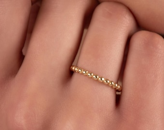 May include: A gold beaded ring on a finger. The ring is made of small, round beads that are evenly spaced.