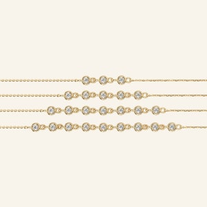 Pu&ograve; includere: Diverse collane sottili in oro, ciascuna ornata da pietre preziose rotonde e trasparenti, sono presentate su uno sfondo neutro. Ogni collana presenta una serie di pietre preziose incastonate lungo una catena sottile, offrendo un design minimalista ed elegante. Queste collane sono probabilmente per donne.