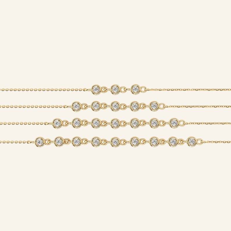 Pu&ograve; includere: Diverse collane sottili in oro, ciascuna ornata da pietre preziose rotonde e trasparenti, sono presentate su uno sfondo neutro. Ogni collana presenta una serie di pietre preziose incastonate lungo una catena sottile, offrendo un design minimalista ed elegante. Queste collane sono probabilmente per donne.
