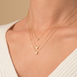 May include: A woman wearing a white sweater with three gold necklaces with small round diamonds.