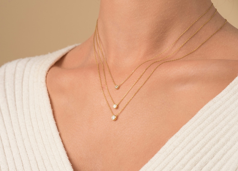 May include: A woman wearing a white sweater with three gold necklaces with small round diamonds.