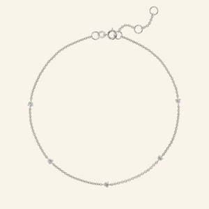 May include: A delicate silver chain anklet with five small, clear gemstones.