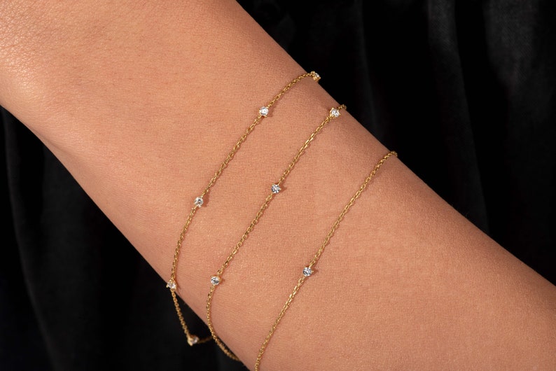 May include: Three delicate gold chains with small clear gemstones spaced evenly along each chain.