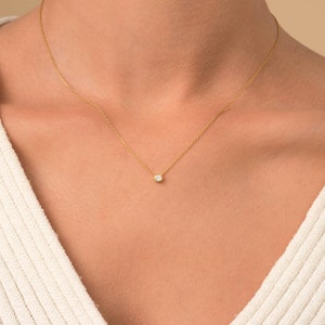 May include: A delicate gold chain necklace with a small, round, clear gemstone pendant.