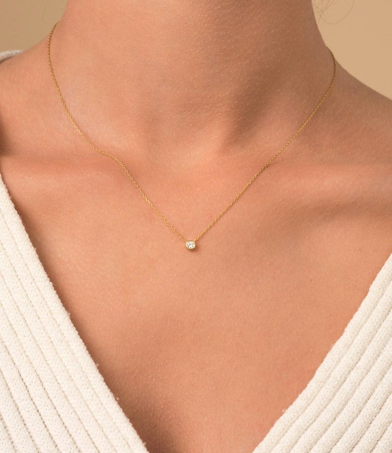 May include: A delicate gold chain necklace with a small, round, clear gemstone pendant.