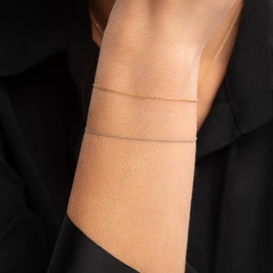 May include: Two delicate chain bracelets, one gold and one silver, worn on a person's wrist.