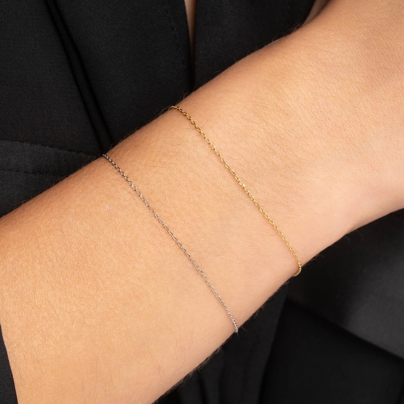 May include: Two delicate chain bracelets on a person's wrist. One bracelet is gold and the other is silver.