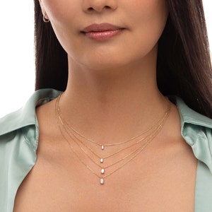 May include: A layered gold chain necklace with three oval-shaped pendants featuring clear gemstones.