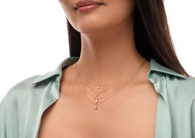 May include: A woman wearing a light green shirt with four gold necklaces with small diamond pendants.