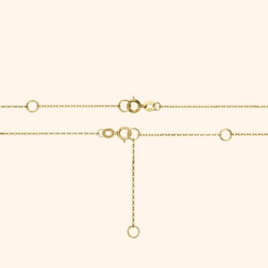 Pu&ograve; includere: Primo piano di due delicate collane d'oro con chiusure regolabili ed estensori di catena. Le collane sono esposte su uno sfondo morbido e neutro, evidenziando i loro dettagli raffinati e la loro maestria artigianale. L'oro ha una finitura calda e lucida.