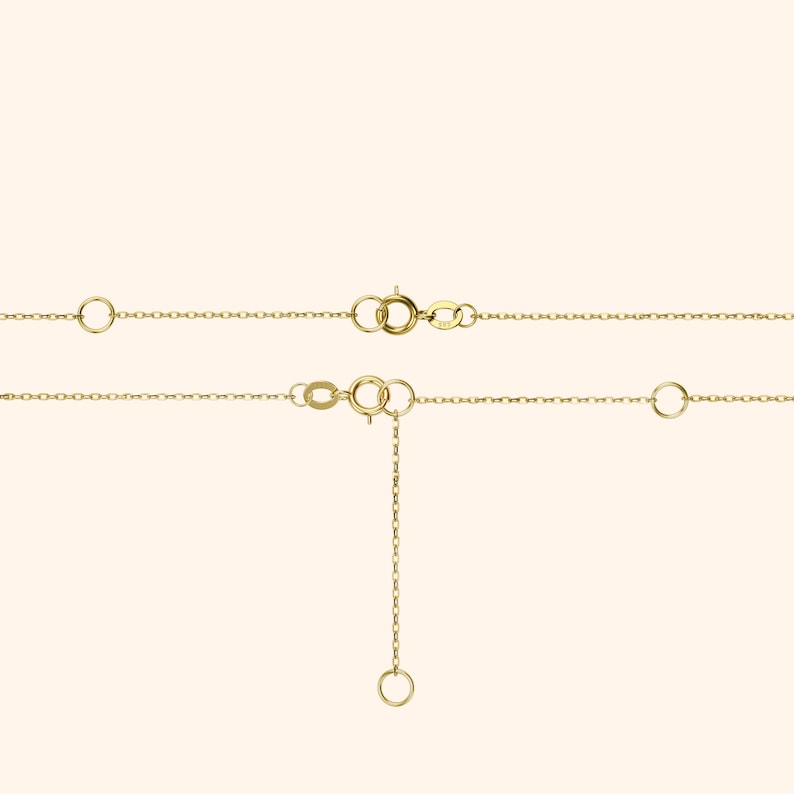 Pu&ograve; includere: Primo piano di due delicate collane d'oro con chiusure regolabili ed estensori di catena. Le collane sono esposte su uno sfondo morbido e neutro, evidenziando i loro dettagli raffinati e la loro maestria artigianale. L'oro ha una finitura calda e lucida.