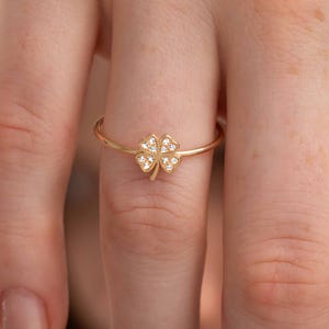 May include: A gold ring featuring a four-leaf clover design with small clear stones.