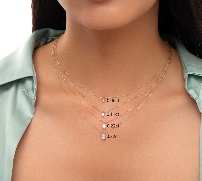 May include: Four gold necklaces with different sized oval-shaped diamonds. The diamonds are labelled with their carat weight: 0.06ct, 0.11ct, 0.22ct, and 0.32ct.