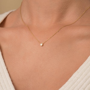 May include: A delicate gold chain necklace with a small, round, clear gemstone pendant.