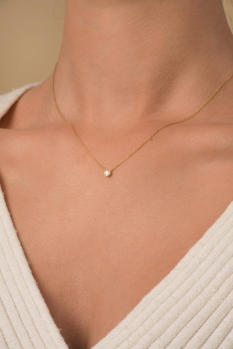 May include: A delicate gold chain necklace with a small, round, clear gemstone pendant.