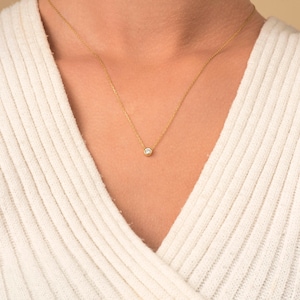 May include: A delicate gold chain necklace with a small, clear gemstone pendant.