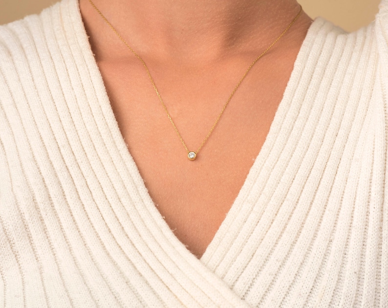 May include: A delicate gold chain necklace with a small, clear gemstone pendant.