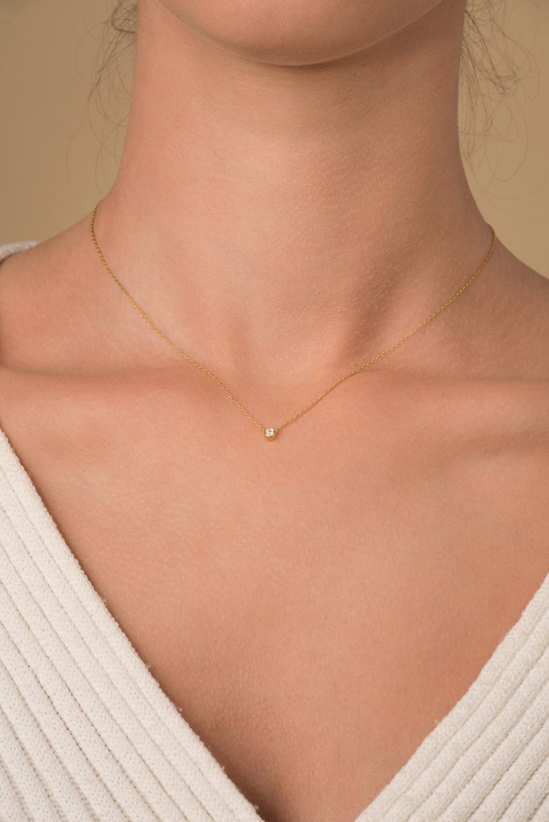 May include: A delicate gold chain necklace with a small, clear gemstone pendant.