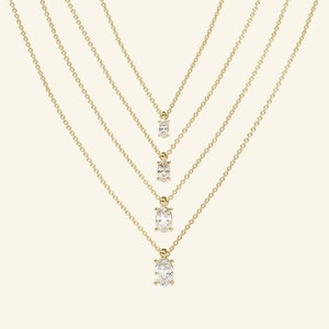 May include: Four gold necklaces with oval-shaped diamond pendants of varying sizes. The necklaces are layered and the pendants are arranged in a graduated pattern.