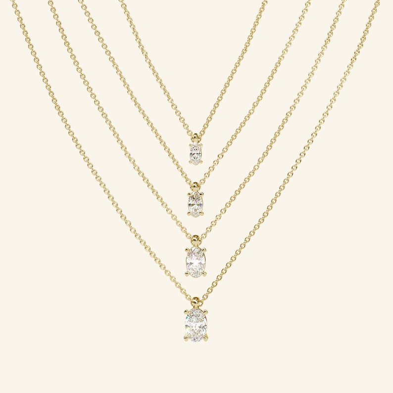 May include: Four gold necklaces with oval-shaped diamond pendants of varying sizes. The necklaces are layered and the pendants are arranged in a graduated pattern.