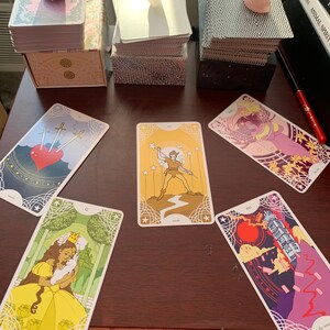 May include: A spread of tarot cards on a wooden table. The cards are from the Animal Spirit deck and include the Three of Swords, Queen of Cups, World, The Tower, and the Star.