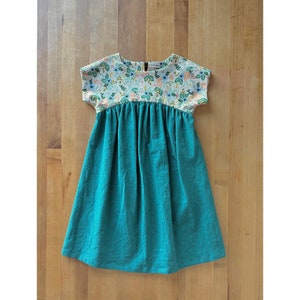 May include: A teal blue dress with a white floral print bodice and short sleeves. The dress has a gathered skirt and is made of a soft, comfortable fabric.