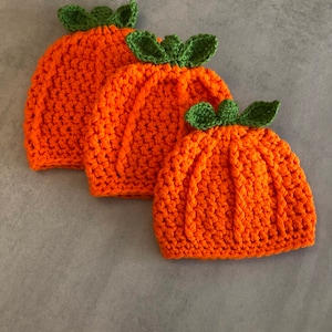 May include: Three crocheted pumpkin hats in different sizes. The hats are orange with green crocheted stems and leaves.