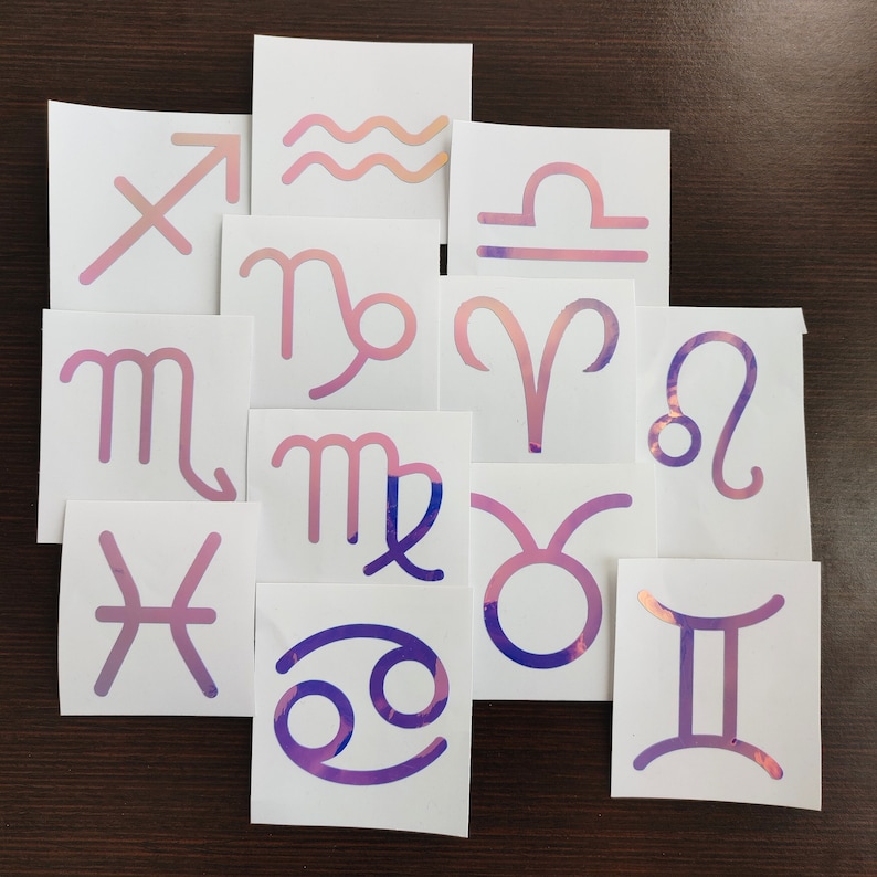 May include: Twelve white cards with holographic pink and purple zodiac symbols. The symbols include Aries, Taurus, Gemini, Cancer, Leo, Virgo, Libra, Scorpio, Sagittarius, Capricorn, Aquarius, and Pisces.
