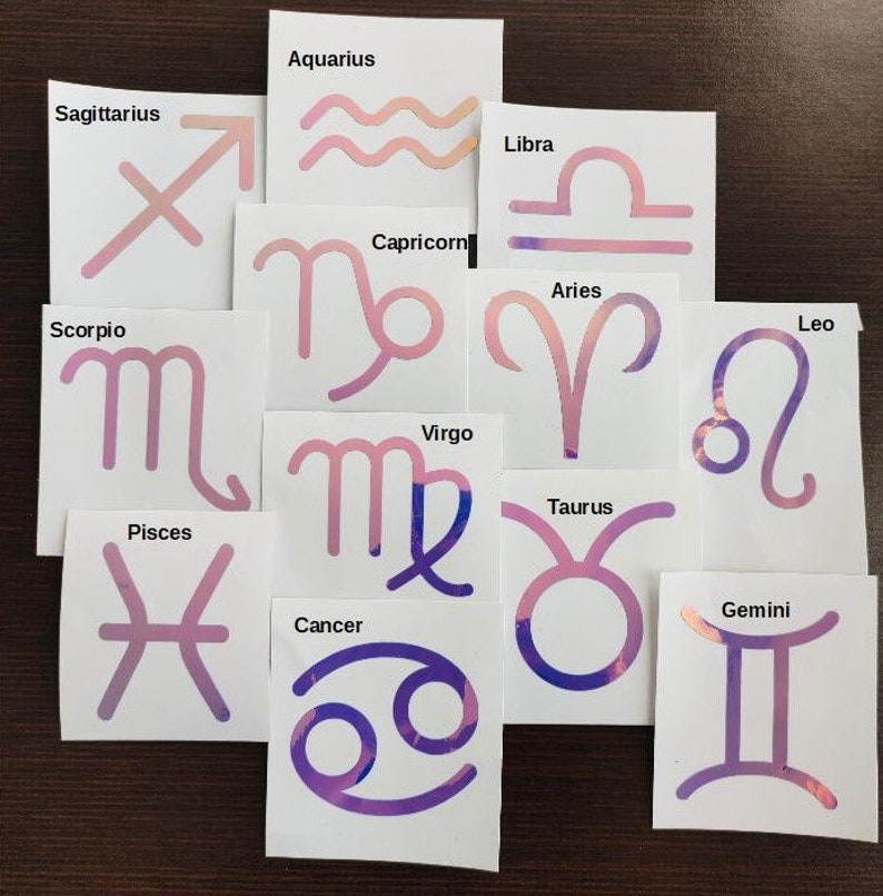 May include: Twelve white cards with pink and purple holographic zodiac signs. Each card features a different zodiac sign with its name printed above it. The signs include: Sagittarius, Aquarius, Libra, Capricorn, Aries, Leo, Scorpio, Virgo, Taurus, Gemini, Pisces, and Cancer.