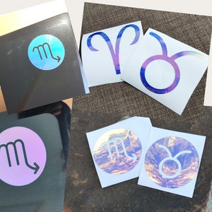 May include: A set of 10 holographic vinyl stickers featuring the zodiac signs: Aries, Taurus, Gemini, Cancer, Leo, Virgo, Libra, Scorpio, Sagittarius, and Capricorn. The stickers are iridescent and have a rainbow effect.