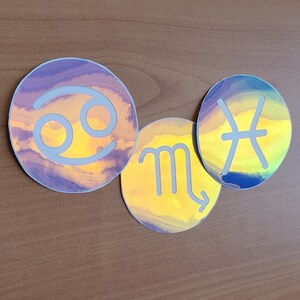 May include: Three iridescent holographic stickers featuring the astrological signs Cancer, Scorpio, and Pisces. The stickers are round and have a white outline.