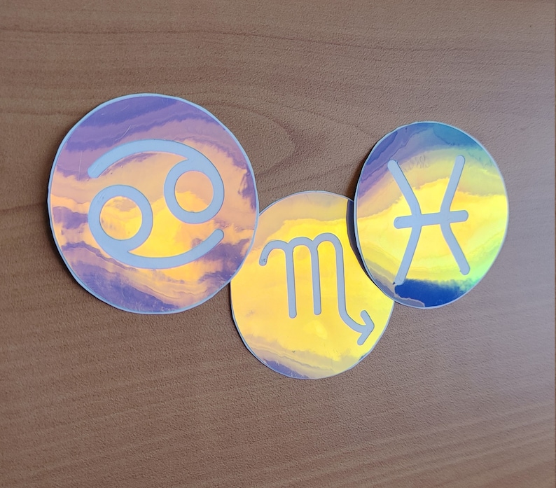 May include: Three iridescent holographic stickers featuring the astrological signs Cancer, Scorpio, and Pisces. The stickers are round and have a white outline.