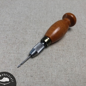 Puede incluir: Una lezna de madera con punta metálica, utilizada para trabajos en cuero o artesanías similares. El mango es de color marrón cálido y los componentes metálicos son plateados. La lezna está diseñada para perforar y crear agujeros.