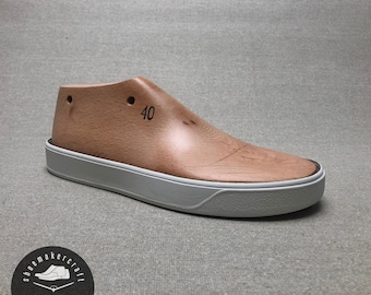Könnte beinhalten: Ein Schuhleisten aus Holz in Größe 40 mit hellbraunem Finish, sitzt auf einer weißen und grauen Sohle. Der Leisten hat zwei kleine Löcher und ist für die Schuhherstellung bestimmt. Das Logo von shoemakercraft befindet sich unten links.