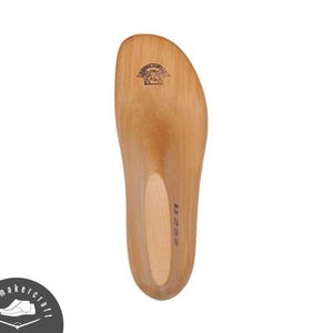 Puede incluir: Plantilla de zapato de madera clara, con un diseño curvado. Presenta un recorte ovalado más claro en el centro y un pequeño emblema en la parte superior. El número "11 22 11" está impreso en el lateral.