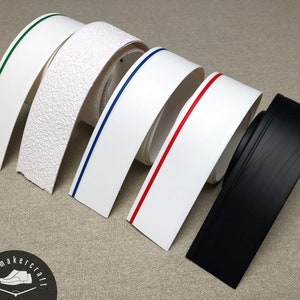 Puede incluir: Surtido de tiras de borde de suela de zapato en varios colores. Incluye tiras blancas con líneas de acento verdes, azules y rojas, una tira blanca texturizada y una tira negra. El logotipo del zapatero es visible.