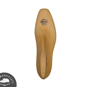 Può includere: Una forma per scarpe in legno, utilizzata nella fabbricazione di calzature, è mostrata su sfondo bianco. La forma marrone chiaro ha una punta arrotondata e un tacco. Un logo è visibile in alto. La taglia è contrassegnata come 6, con le misure 26/28. La forma misura circa 26 cm di lunghezza.