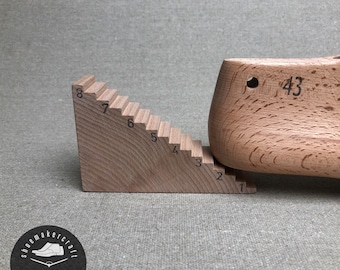 Könnte beinhalten: Ein Holzschuhleisten mit der Nummer 43 und ein Holz-Treppenmesswerkzeug. Das Treppenwerkzeug hat die Zahlen 1 bis 8. Die Objekte sind aus hellem Holz gefertigt und werden zur Schuhherstellung verwendet.