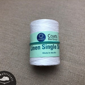Puede incluir: Un carrete de hilo de lino blanco, etiquetado como "Linen Single S" por Coats Barbour. El carrete está envuelto con una etiqueta turquesa y una banda elástica verde. También se ve el texto "Made in the EU".