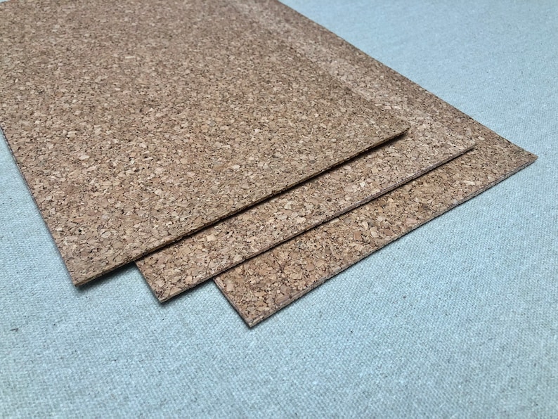 K&ouml;nnte beinhalten: Drei rechteckige Korkplatten mit einer nat&uuml;rlichen, strukturierten Oberfl&auml;che sind &uuml;bereinander gestapelt. Der Kork hat ein gesprenkeltes, hellbraunes Aussehen. Die Platten sind diagonal angeordnet, wobei die oberste Platte die anderen leicht &uuml;berlappt.