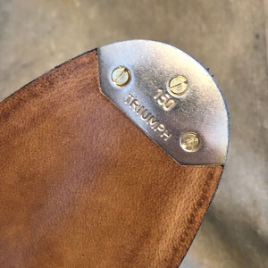 Puede incluir: Primer plano de una suela de zapato de claqu&eacute; de cuero marr&oacute;n con una puntera de metal plateado. La puntera est&aacute; asegurada con tornillos de lat&oacute;n y presenta la palabra "TRIUMPH" y el n&uacute;mero "150".