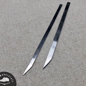 Peut inclure: Deux outils métalliques de fabrication de chaussures avec des extrémités pointues et tranchantes. L'un est droit, l'autre incurvé. Les outils sont sur une surface texturée de couleur neutre. Un logo circulaire avec du texte et un graphique de chaussure est dans le coin inférieur gauche.