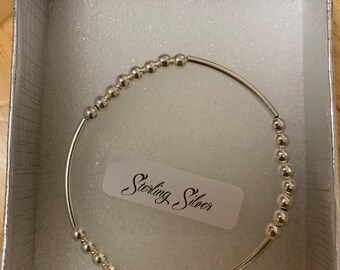 Puede incluir: Un brazalete de plata con cuentas y una etiqueta de plata de ley que dice "Sterling Silver". El brazalete está en una caja blanca con un forro de espuma blanca.