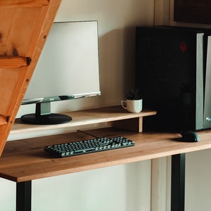 May include: A wooden desk with a black computer tower, a monitor, a keyboard, and a mouse. The desk has a shelf for the monitor and a black adjustable leg.